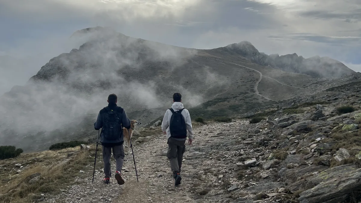 Dos senderistas con bastones caminando entre nubes en montaña